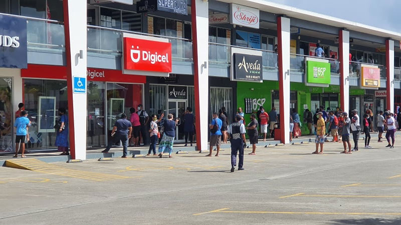 Police officers ensure there is control outside Vodafone and Digicel outlets as people rush to get the $50 Government assistance 